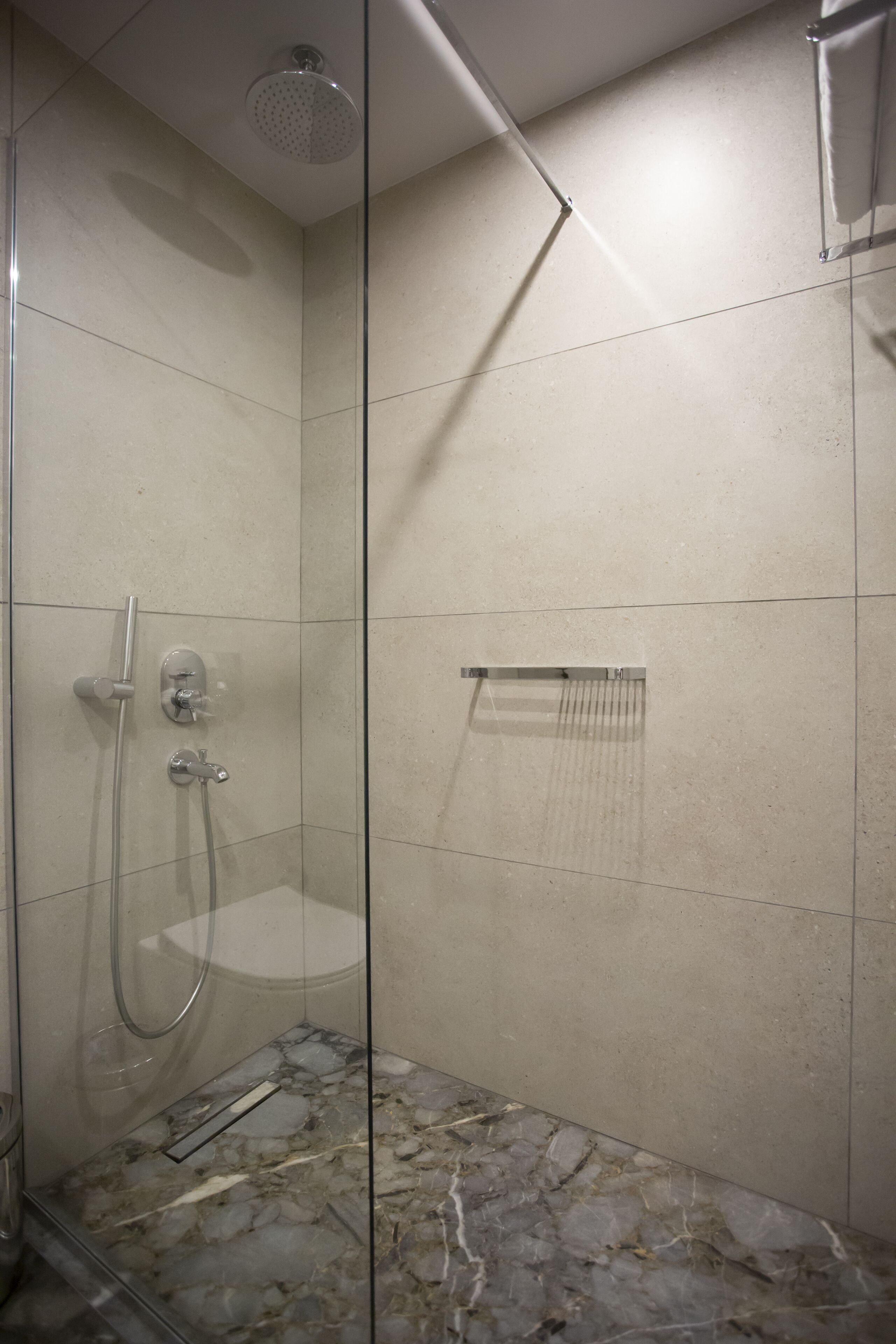 Une douche fermée par des parois de verre, avec un sol en marbre, un porte-serviettes et une pomme de douche.