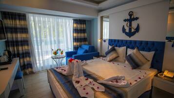 Quarto de hotel com uma cama, um sofá azul, uma mesinha com um vaso e uma janela grande com cortinas.