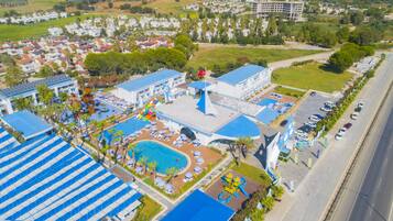 An aerial view of a resort with multiple swimming pools, sun loungers, and a large water slide.