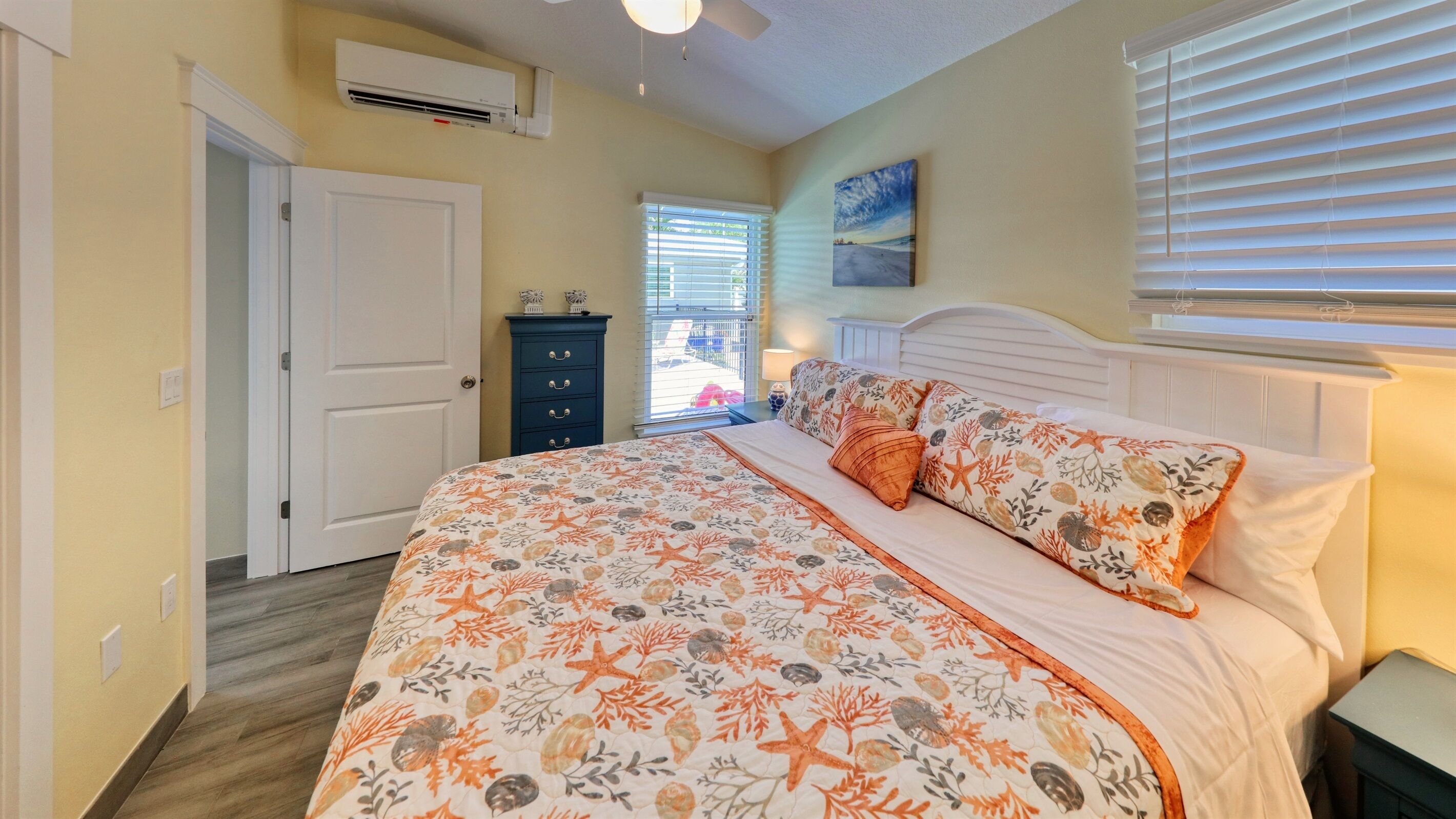 A bedroom with a bed, a dresser, a window with blinds, and an air conditioning unit.