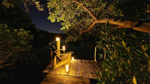 A wooden dock with a bench and candles, surrounded by dense foliage and a calm body of water at night. - Resort-Style Ground Floor 3BR Manatee Suite, Heated Pool / Spa, Lakefront (Anna Maria)