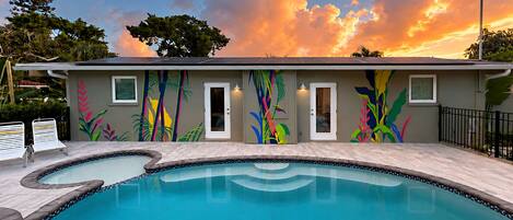A pool area with a mural, a pool, and a building with doors and windows.