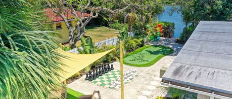 A garden with a chessboard, a pool, and a house with a red roof.