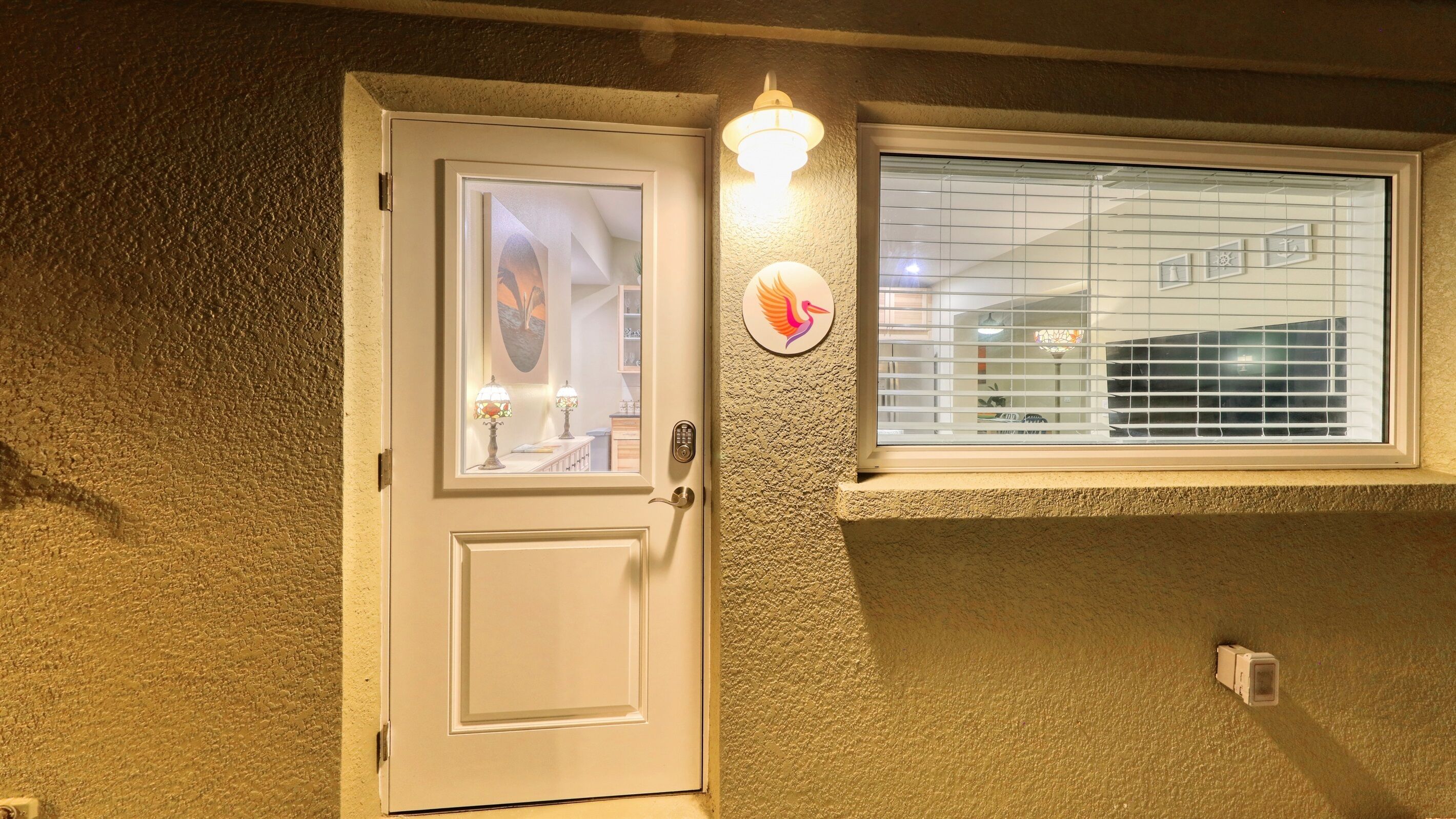 Een witte deur met een ruit, een wandlamp en een raam met zonwering.