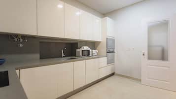 A modern kitchen with white cabinets, a stainless steel sink, a microwave, and an oven.