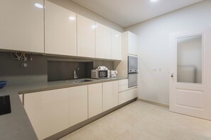 A modern kitchen with white cabinets, a stainless steel sink, a microwave, and an oven. - Basil Red Apartment, AC, Wifi !new! (Lisboa)