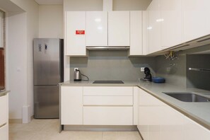 Una cocina moderna con armarios blancos, un refrigerador de acero inoxidable, una tetera y un lavamanos.