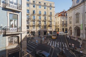 A street view with a tram, pedestrians, and buildings with balconies.