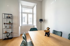 A room with a wooden table, green upholstered chairs, a black metal shelf with decorative items, a window with white frames, and a floor lamp. - Basil Red Apartment, AC, Wifi !new! (Lisboa)