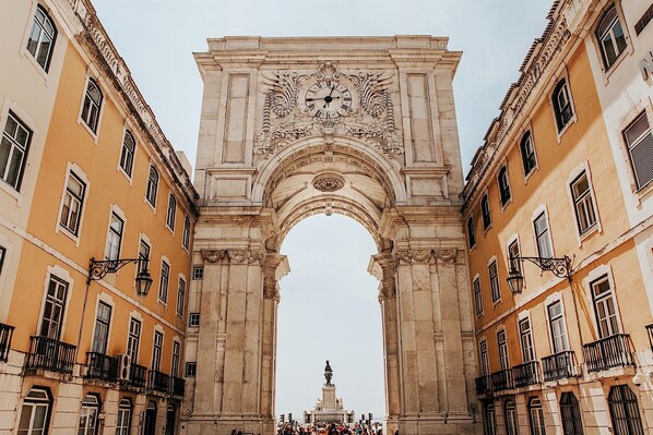 An ornate stone archway with a clock, flanked by buildings with balconies and windows.