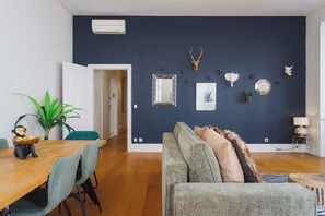 A modern living room with a dark blue accent wall, a wooden dining table, a grey sofa, and a variety of wall-mounted decorative items.