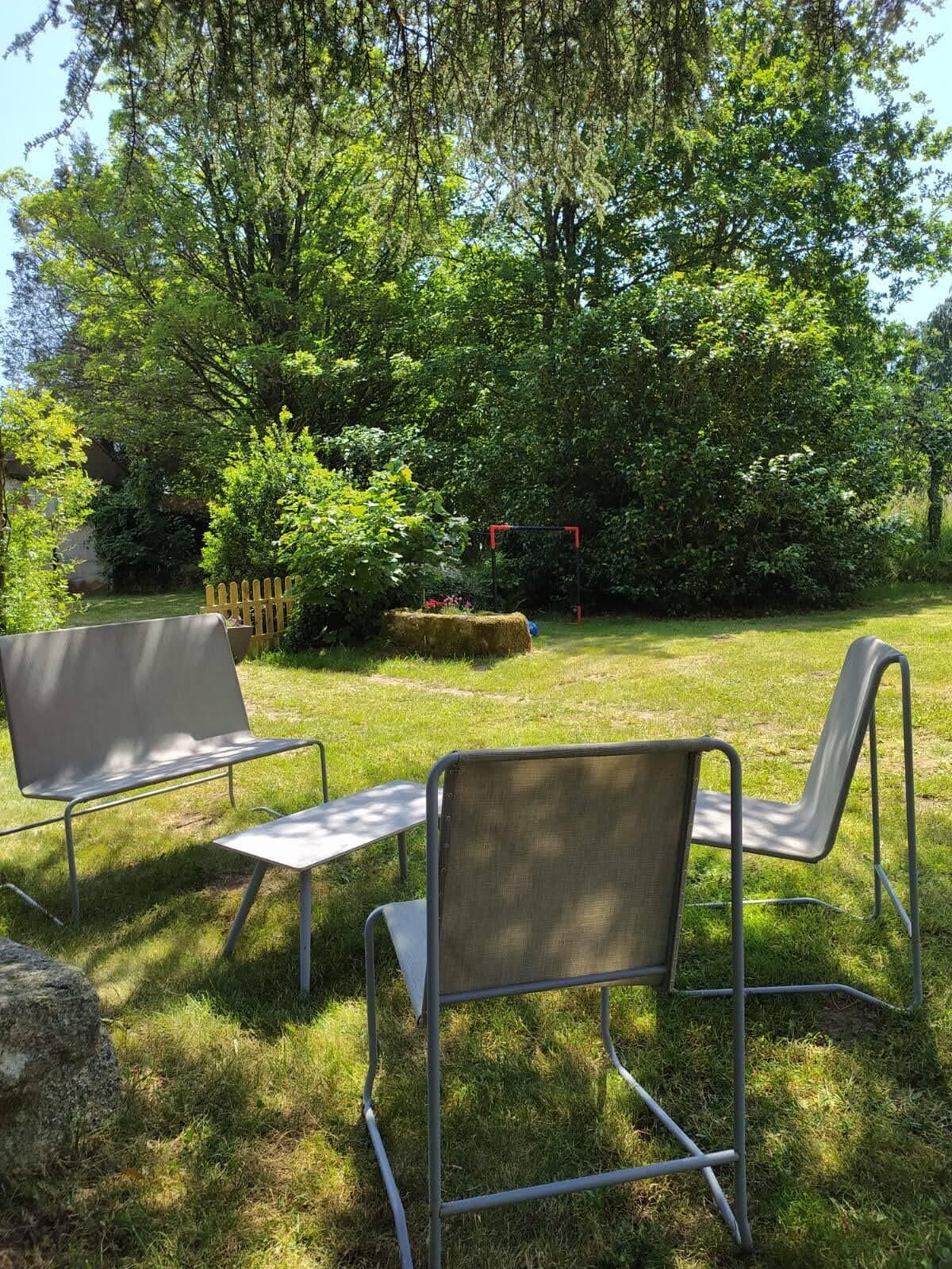 Zona esterna con sedute in metallo, tavoli e rigogliosa vegetazione.