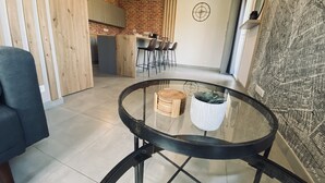 Una cocina moderna con armarios de madera, una zona de comedor con mesa de vidrio y un espacio de estar con sofá y mesa auxiliar.