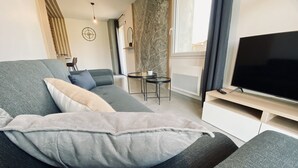 Una sala moderna con un sofá gris, un televisor de pantalla plana y una mesita.