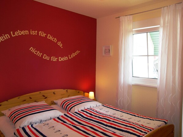 A bedroom with a red wall, a bed with striped bedding, and a window with curtains.