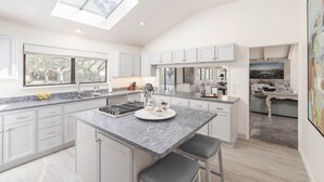 A modern kitchen with a skylight, white cabinetry, a marble countertop, and a central island with bar stools. - 3819 Casa Carmela - Private Home in Carmel (Carmel)