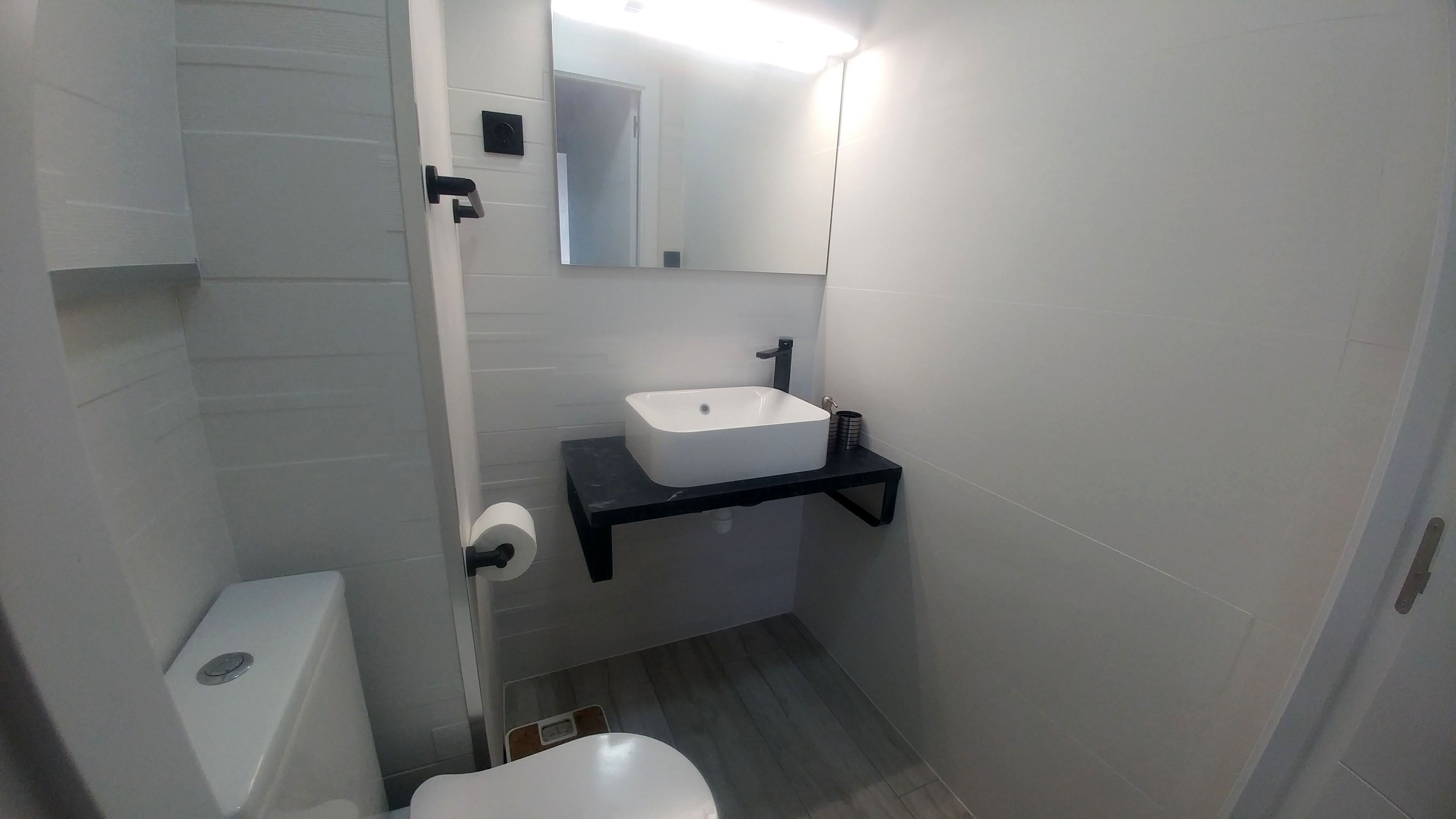 A small, modern bathroom with a white toilet, a white sink on a black countertop, and a mirror above the sink.