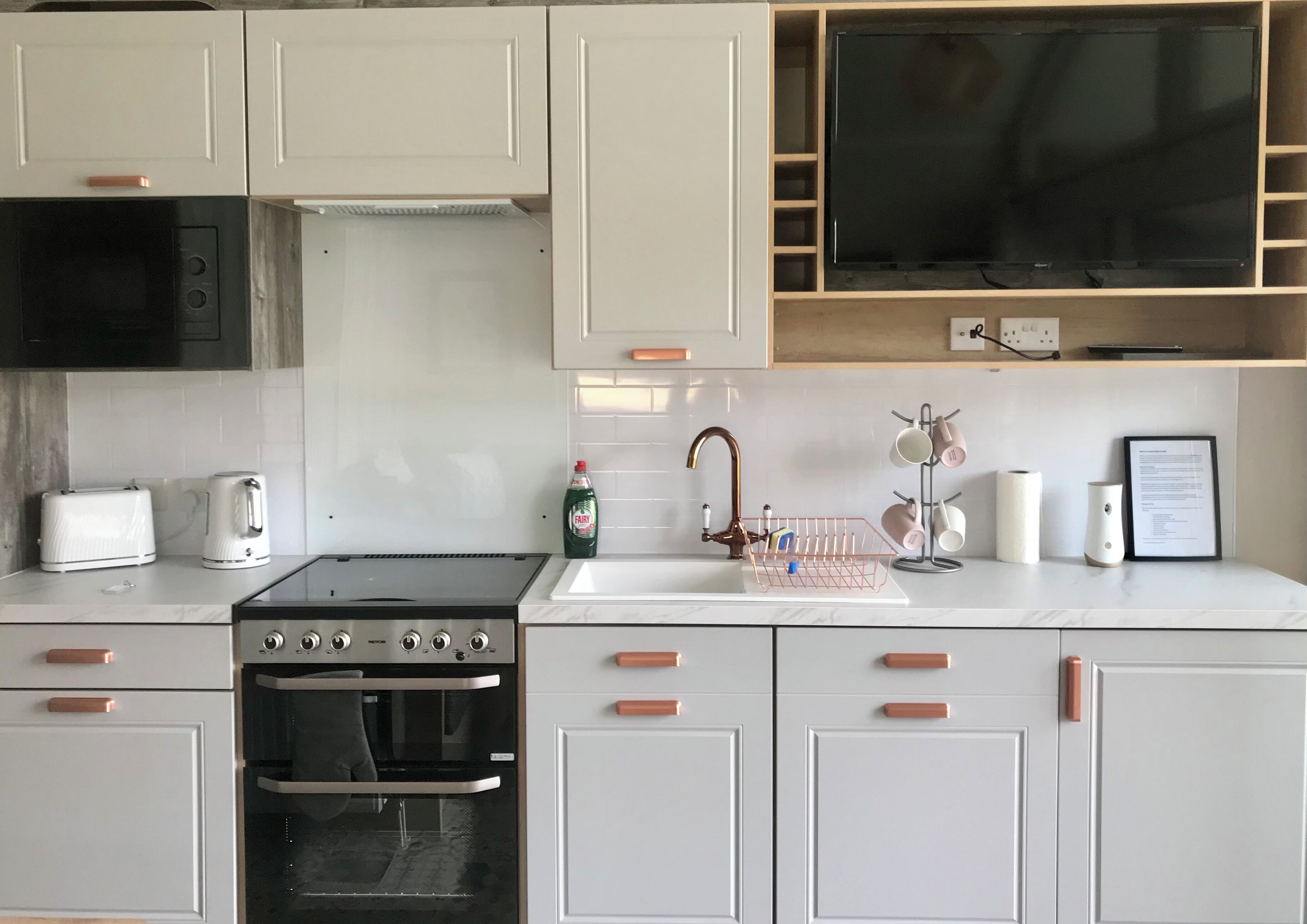 A modern kitchen with white cabinets, a black stove, a microwave, a sink with a faucet, and a TV mounted above the counter.