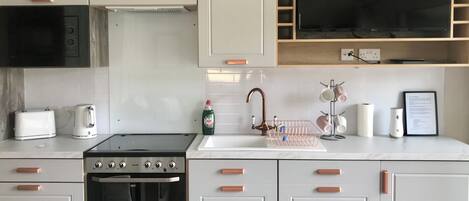 A modern kitchen with white cabinets, a black stove, a microwave, a sink with a faucet, and a TV mounted above the counter.