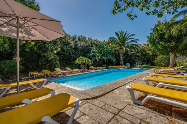 A poolside area with lounge chairs and a large umbrella. - S'Heretat Historic Estate (Capdepera)