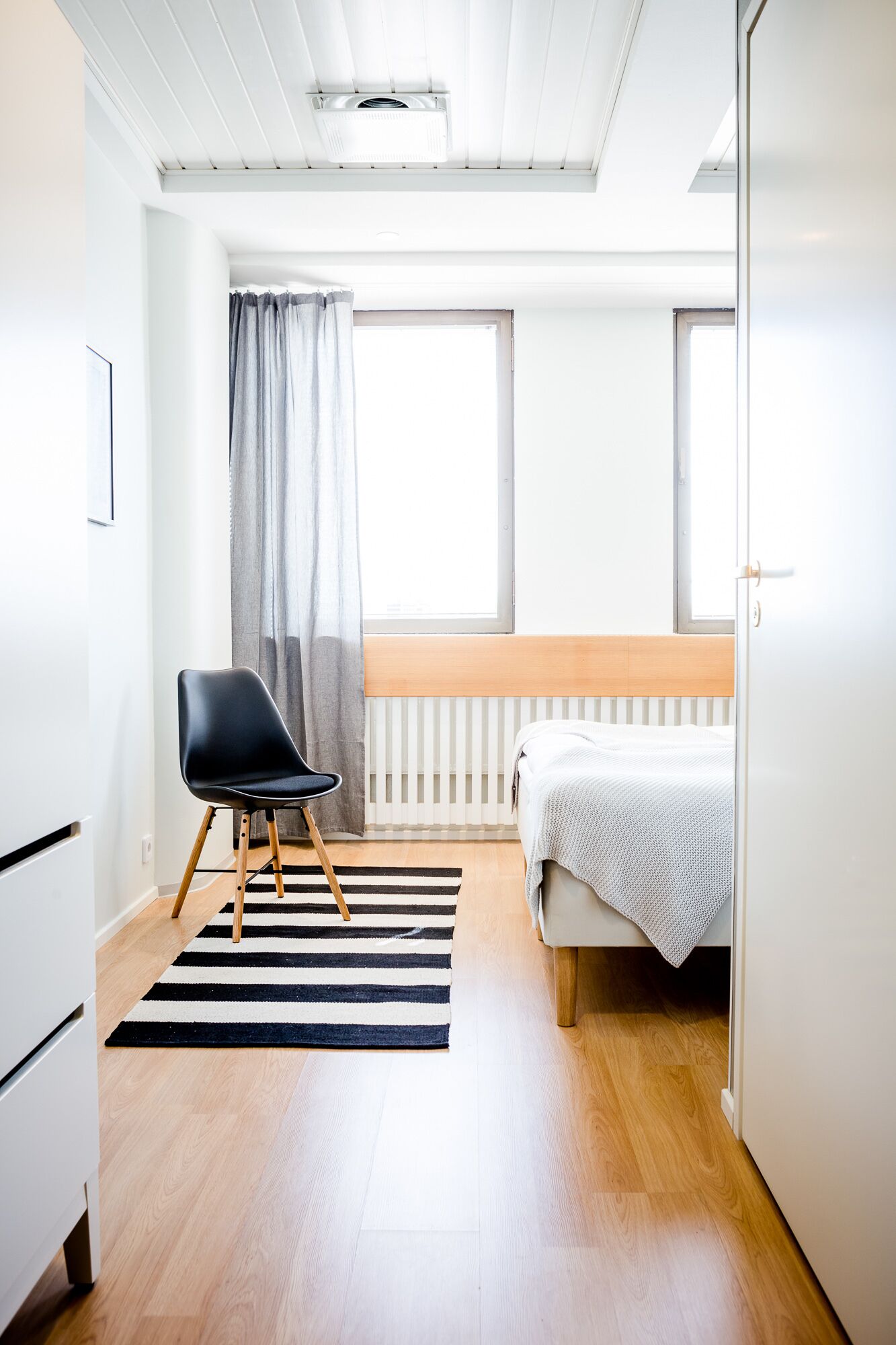 Un dormitorio moderno con cama, una silla, un radiador y una ventana.