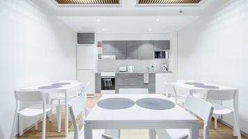 Una cocina moderna con armarios blancos, un microondas y una estufa. Hay dos mesas de comedor blancas con sillas, y un techo con detalles de madera.