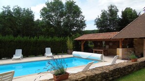 Une piscine avec des chaises longues, un mur en pierre et un patio couvert.