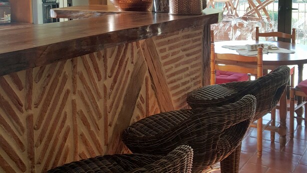 Un espace bar avec des chaises en osier, un comptoir en bois et des verres suspendus.