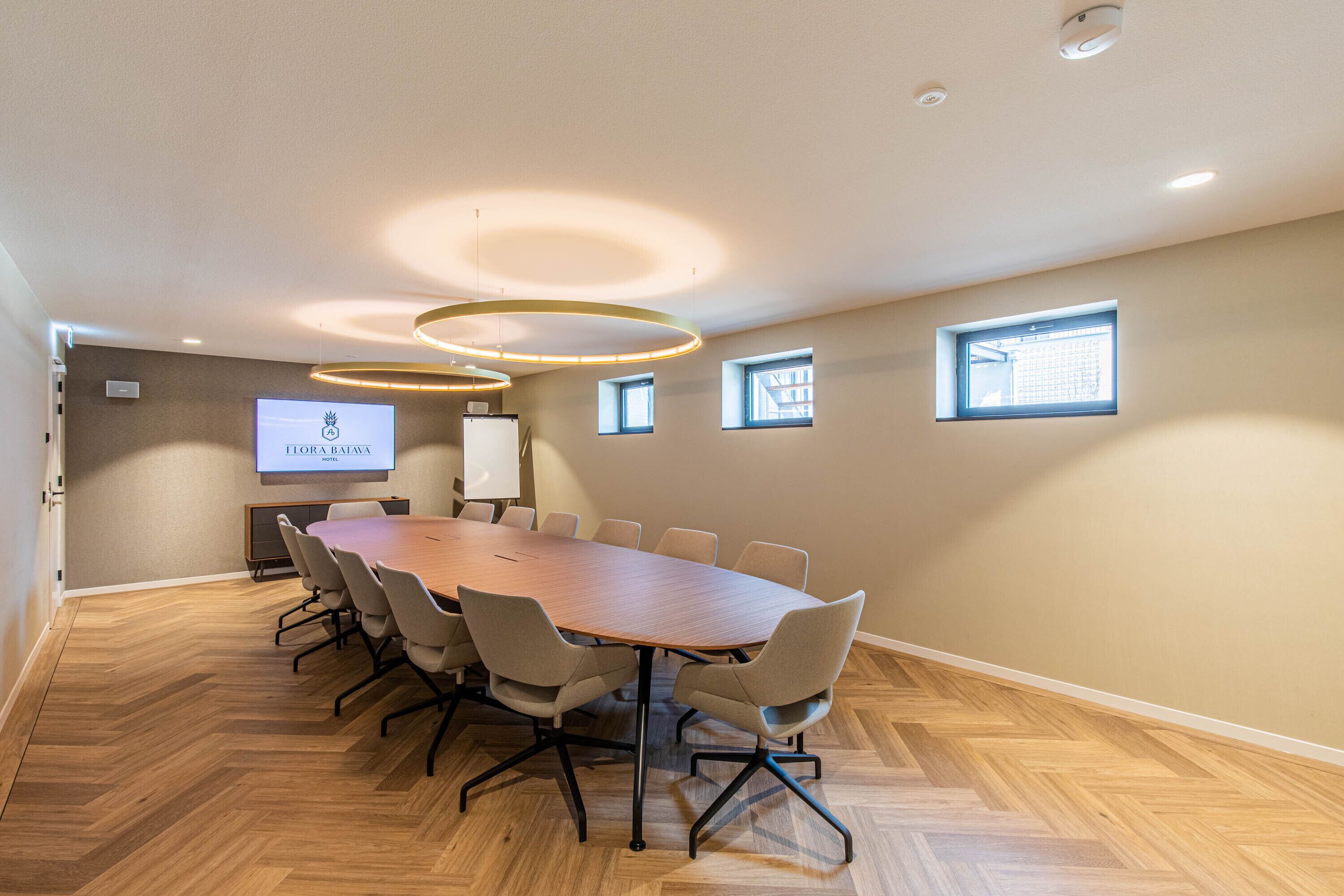 Una sala de conferencias con una gran mesa, sillas, una pantalla de proyector y una ventana.