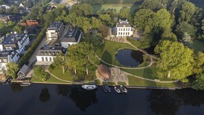 An aerial view of a residential area with a large house, a pond, and boats docked at a pier. - Hotel Flora Batava (Nieuwersluis)