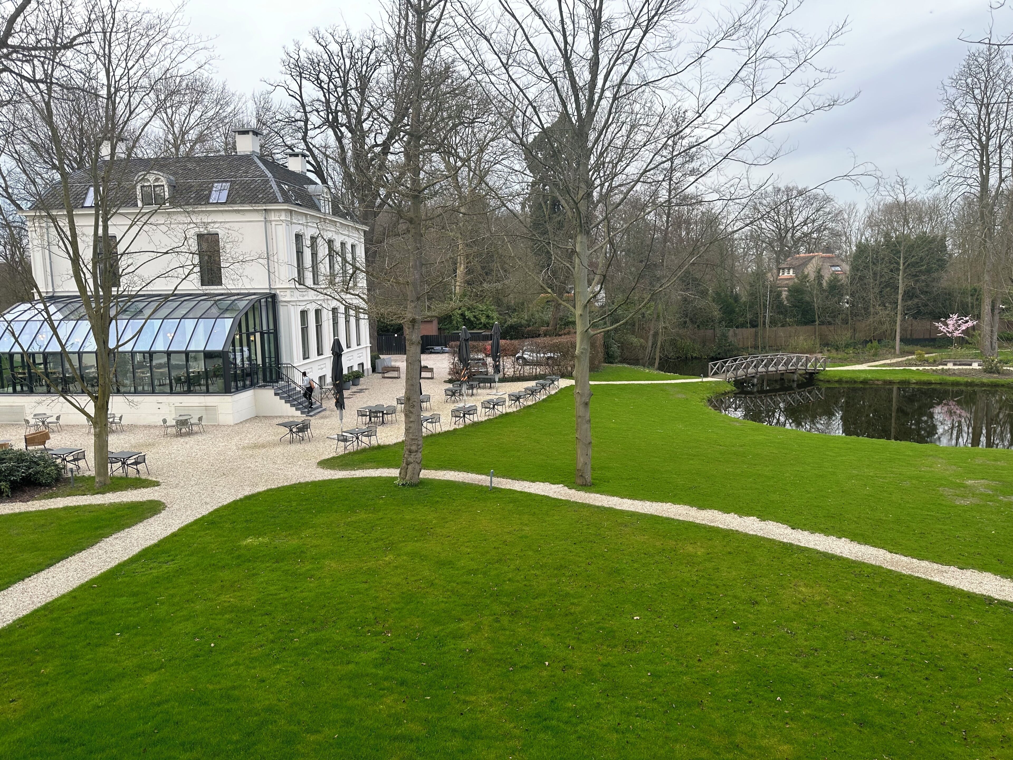 A white building with a glass conservatory, outdoor seating, and a pond.