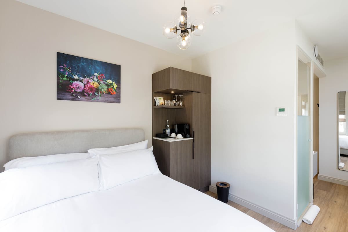 A bedroom with a bed, a painting of flowers, a wardrobe, a coffee machine, and a mirror.