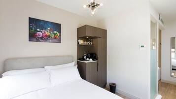 A bedroom with a bed, a painting of flowers, a wardrobe, a coffee machine, and a mirror.