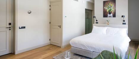 A bedroom with a bed, bedside tables, a round dining table with cutlery, a vase with flowers, and a painting on the wall.