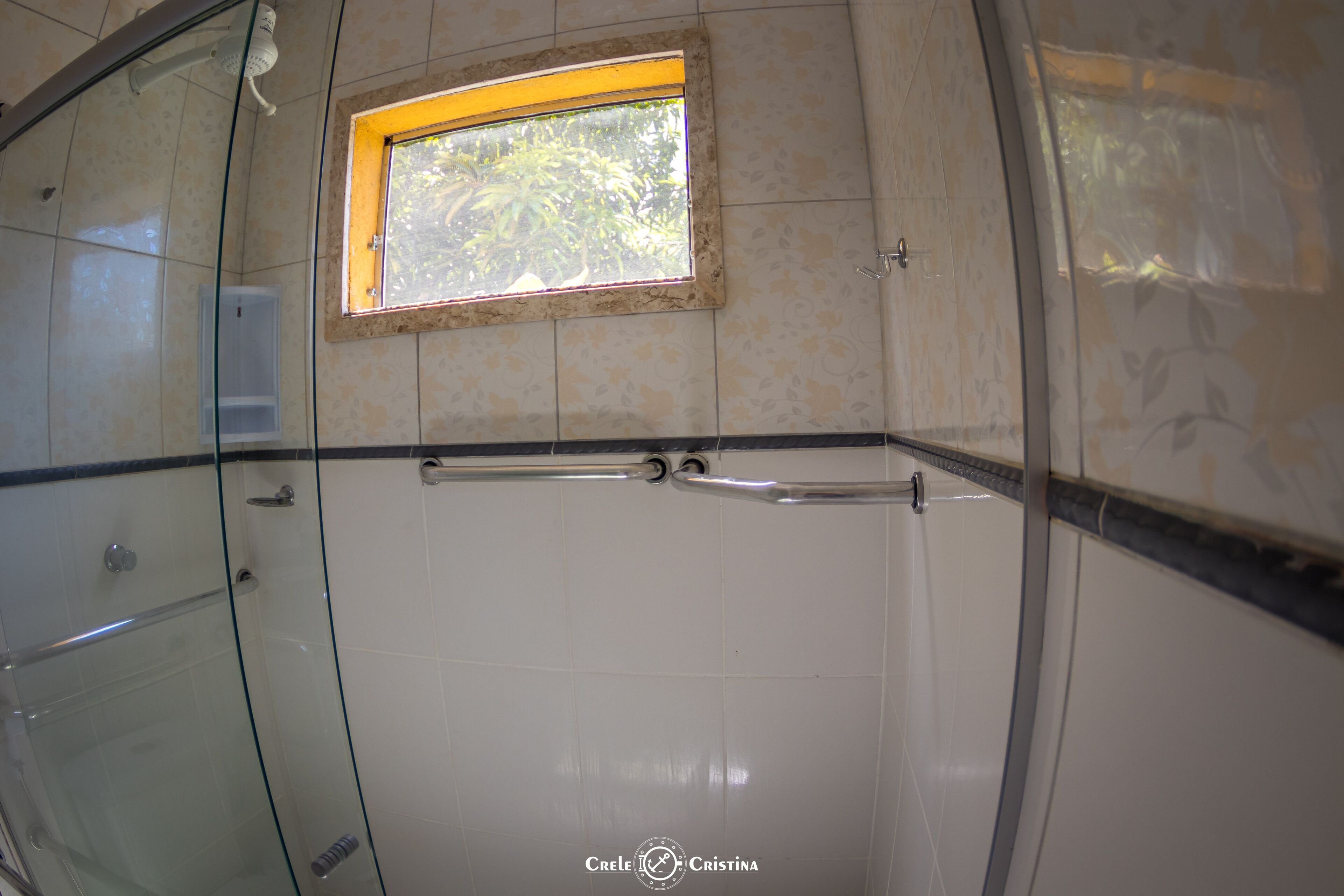 A bathroom with a glass shower enclosure, a small window with a view of trees, and tiled walls.