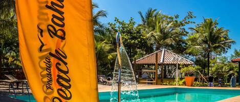 Una bandera con la inscripción "Pousada Beach Bahia", una piscina y una fuente de agua.