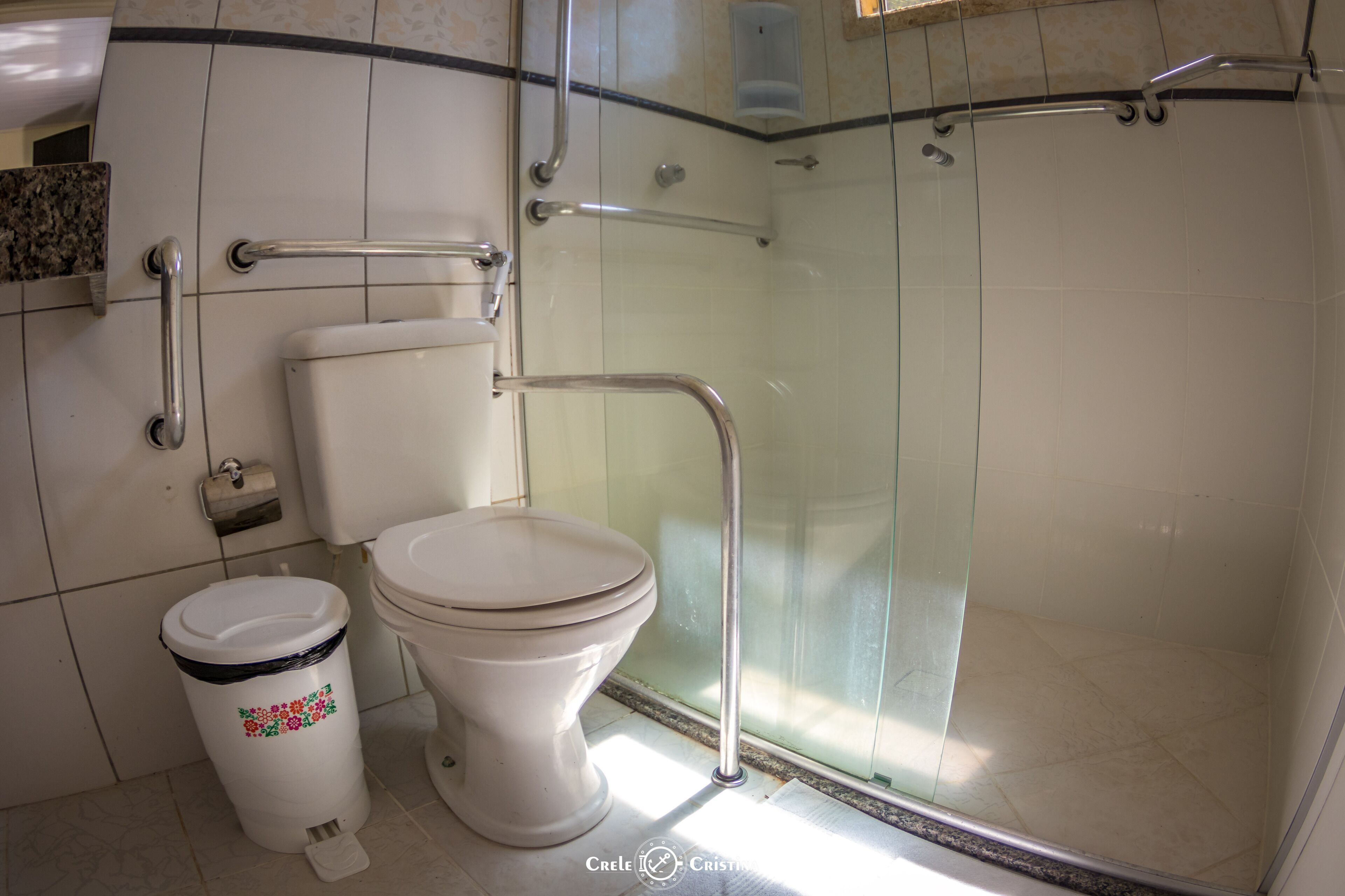 A bathroom with a toilet, a trash can, and a glass shower enclosure.