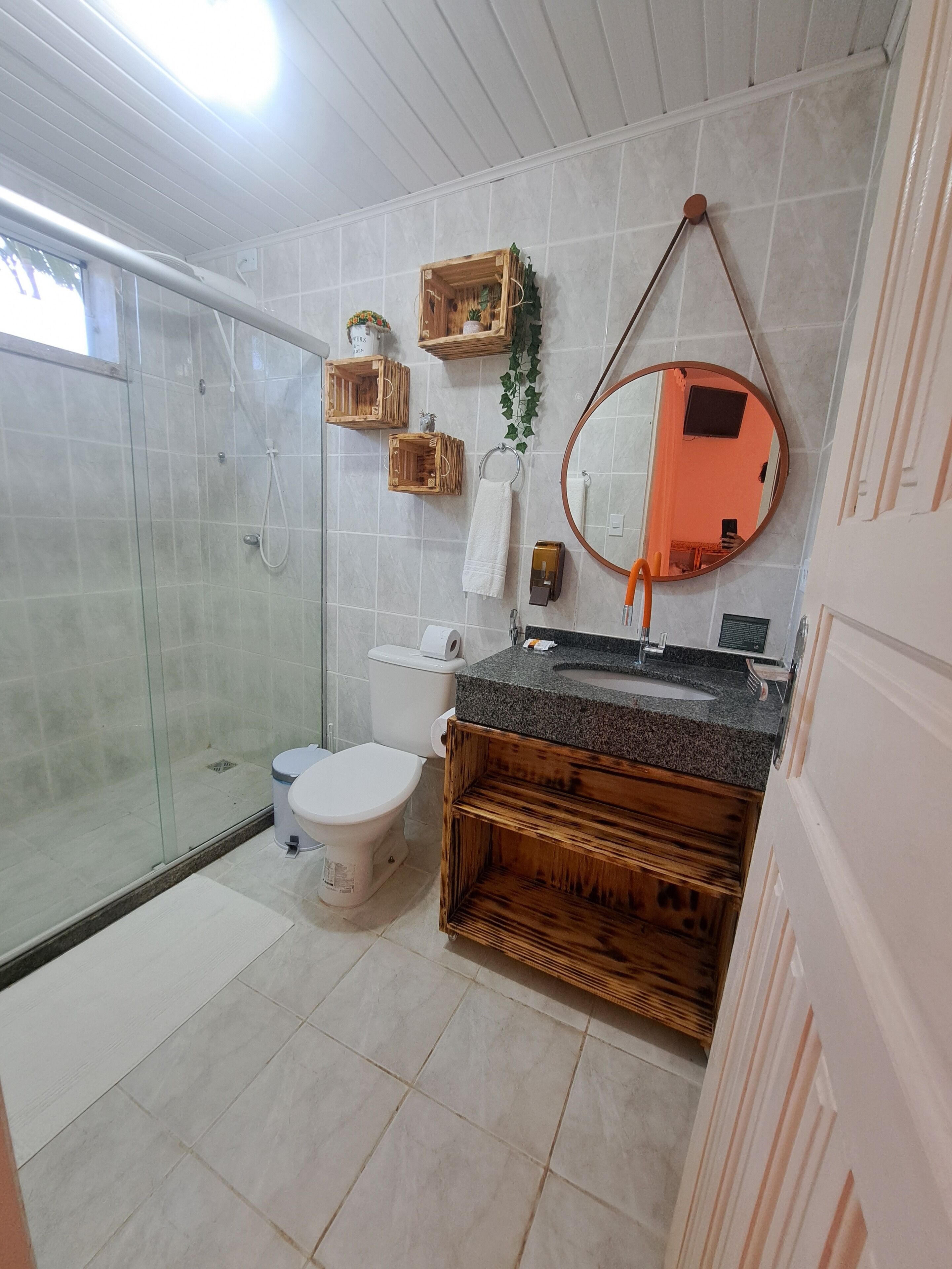 Ein Badezimmer mit Duschkabine aus Glas, Toilette, Waschbecken mit Holzschrank und Spiegel.