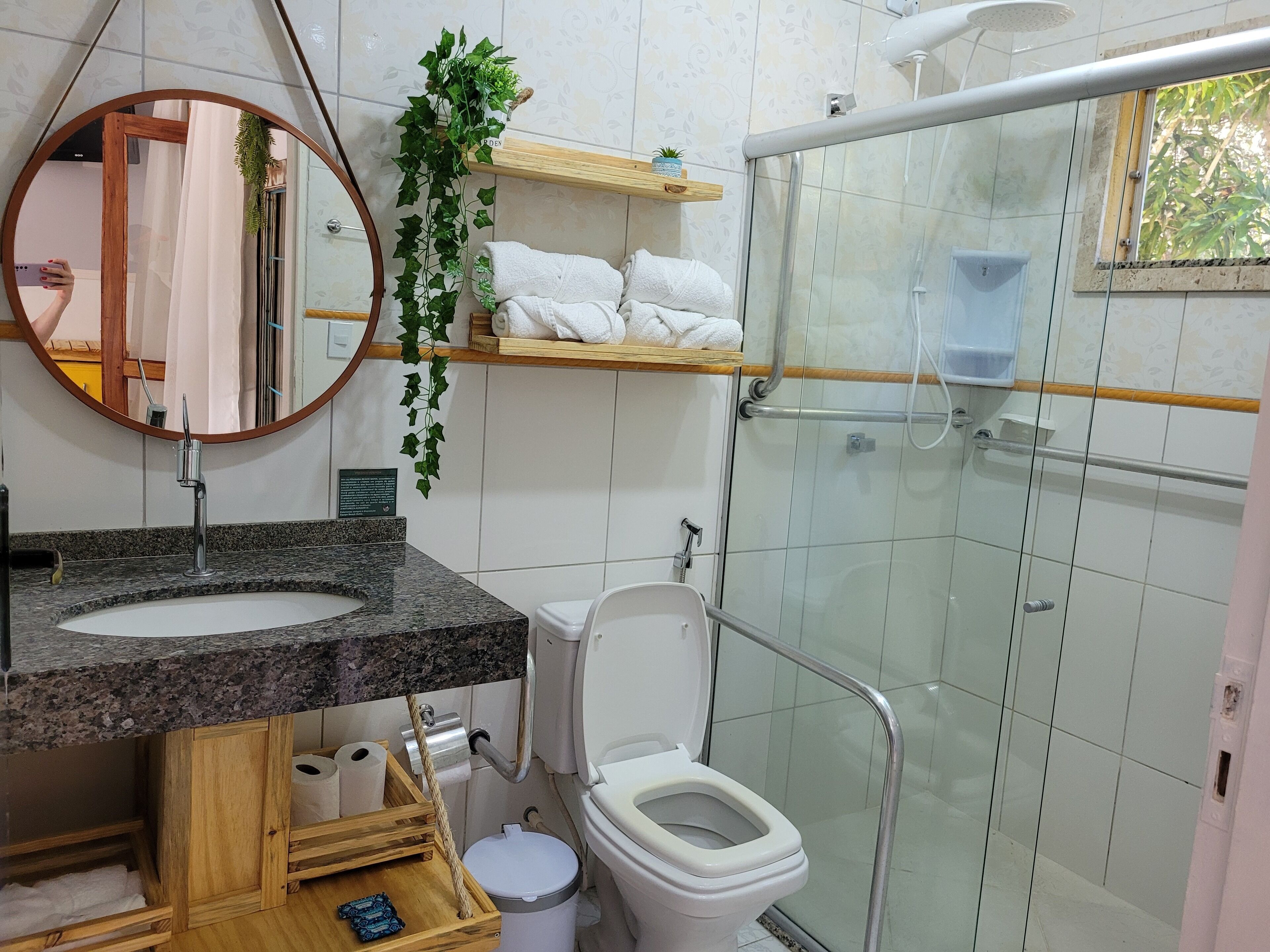 A bathroom with a granite sink, a toilet, a glass shower enclosure, and a mirror with a wooden frame.