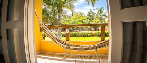 A hammock in a yellow room with a view of a garden.