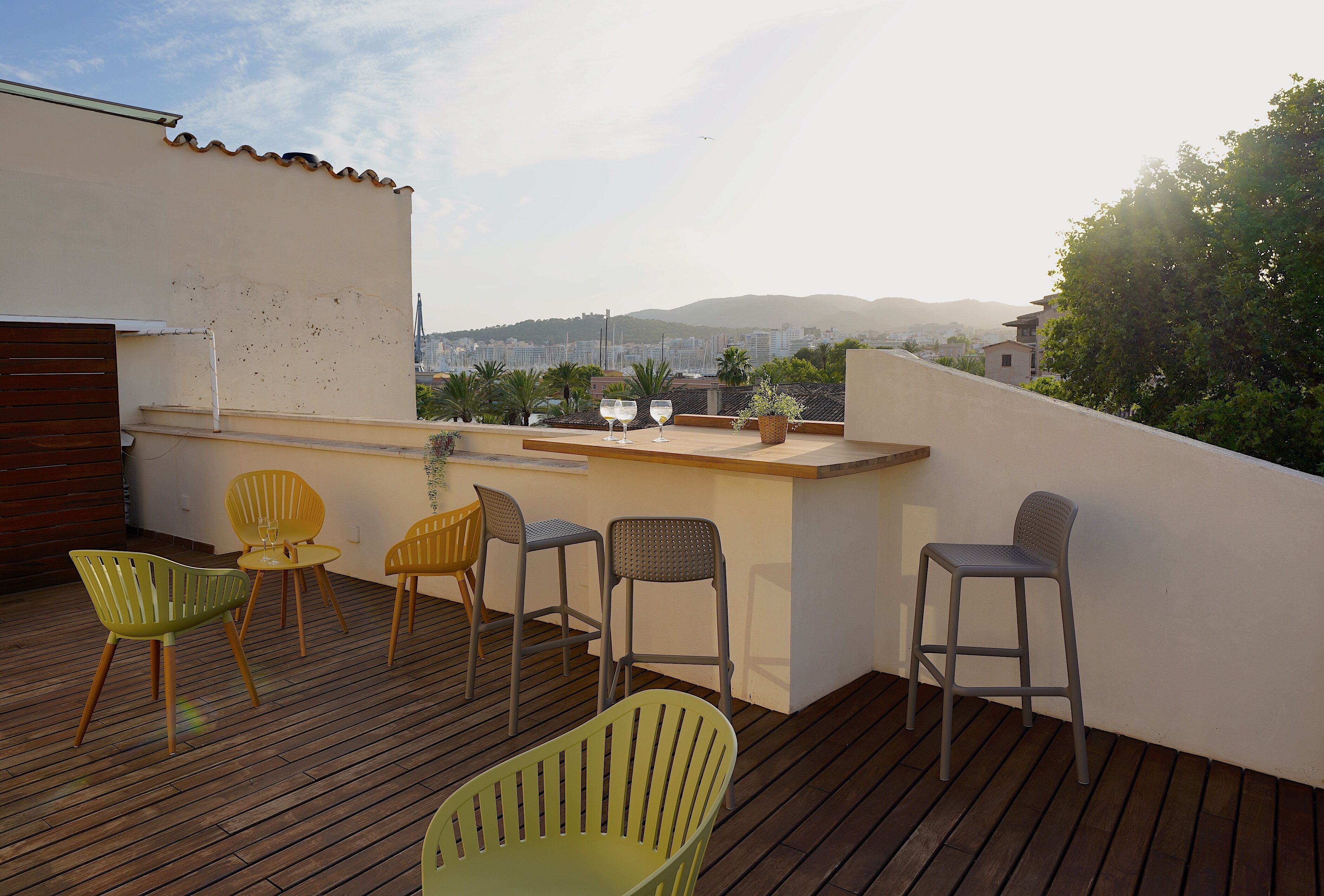 A rooftop terrace with wooden flooring, a bar area, and several chairs.