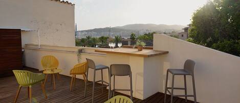 A rooftop terrace with wooden flooring, a bar area, and several chairs.