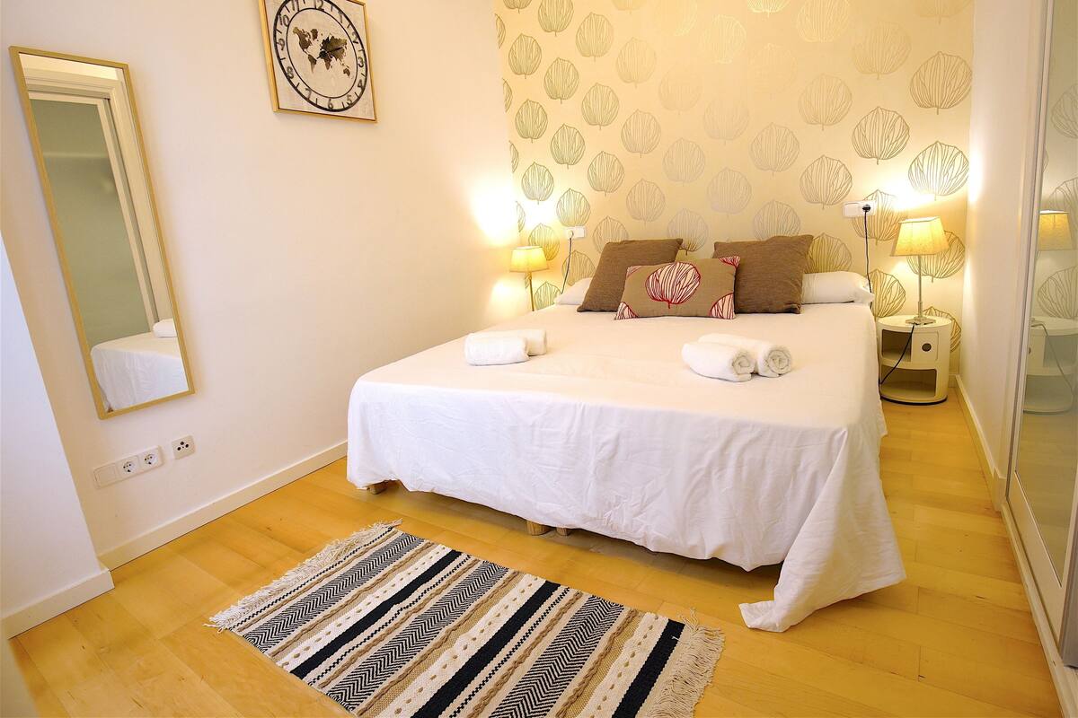 Un dormitorio ordenado con una cama grande, lámparas de noche, un espejo y un papel tapiz estampado.