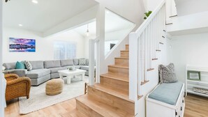 Un salon spacieux avec un canapé d’angle gris, une table basse blanche et un escalier en bois.