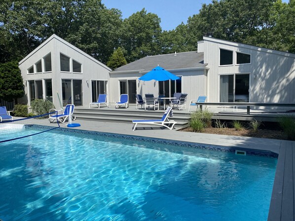A modern house with a swimming pool, blue lounge chairs, and a covered patio area.