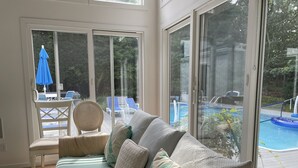 A sunlit room with a large sliding glass door leading to a pool area, featuring a sofa and chairs. - East Hampton SPECIAL (East Hampton)