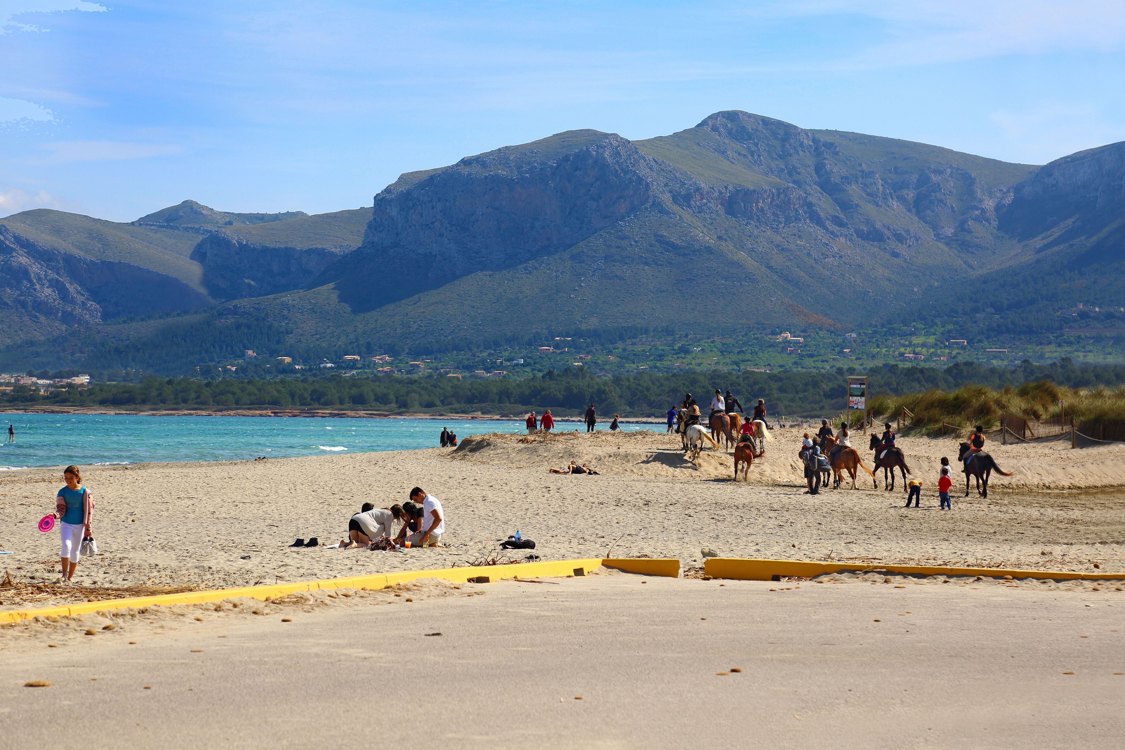 A beach with people, horses, and a mountainous backdrop.