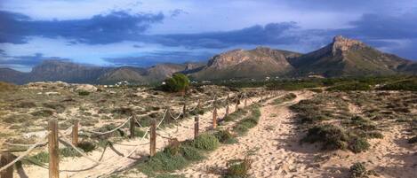 A sandy path with wooden posts and ropes, leading towards a mountainous landscape.