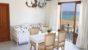 Een kamer met een bed, een eettafel met stoelen, een kroonluchter en uitzicht op de zee door een groot raam.