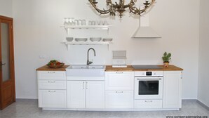 Een keuken met witte kasten, een dubbele spoelbak, een fornuis en een kroonluchter.